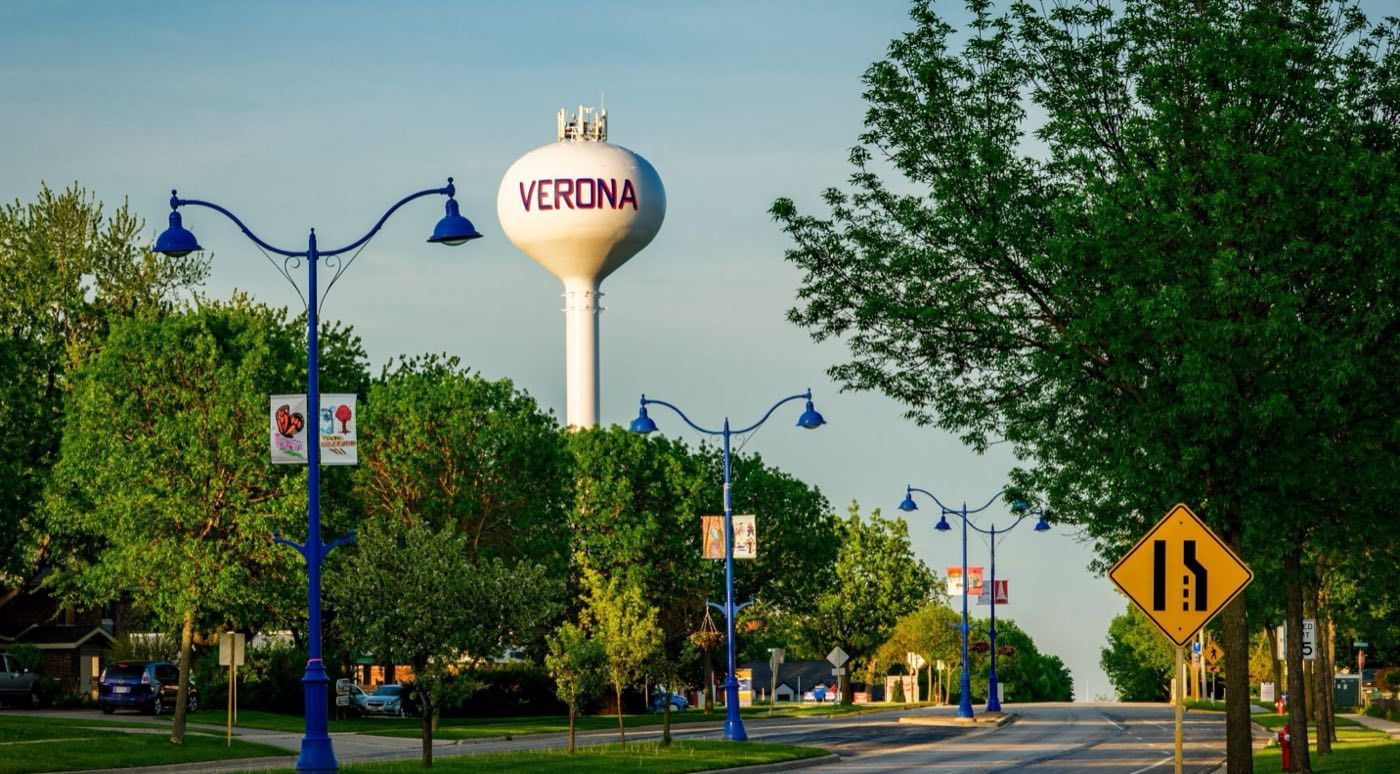 The Verona water tower rising above a residential street lined with blue lampposts and summer trees.